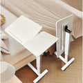 White adjustable overbed laptop table beside a sofa and bed with wheels