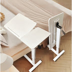 White adjustable overbed laptop table beside a sofa and bed with wheels
